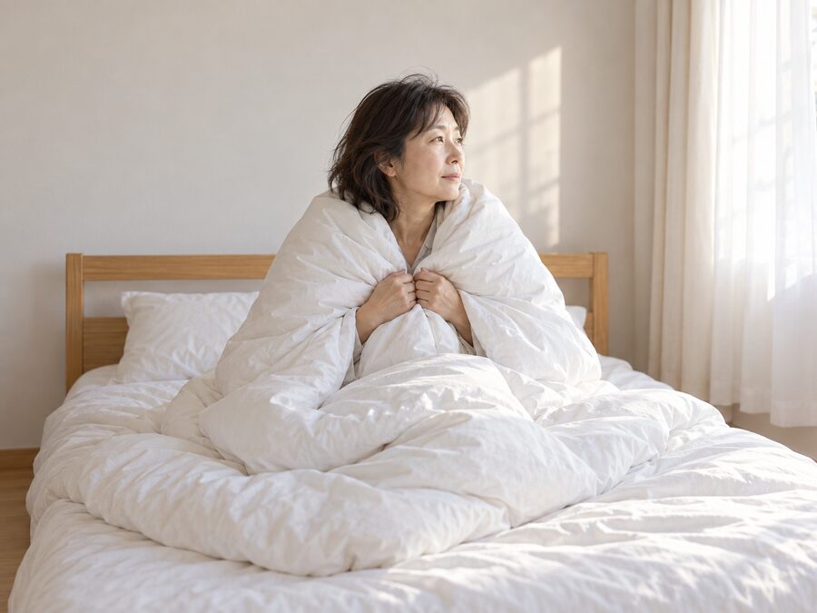 ベッドの上で起き上がり、羽毛ふとんを肩からはおって窓の外を見ている女性